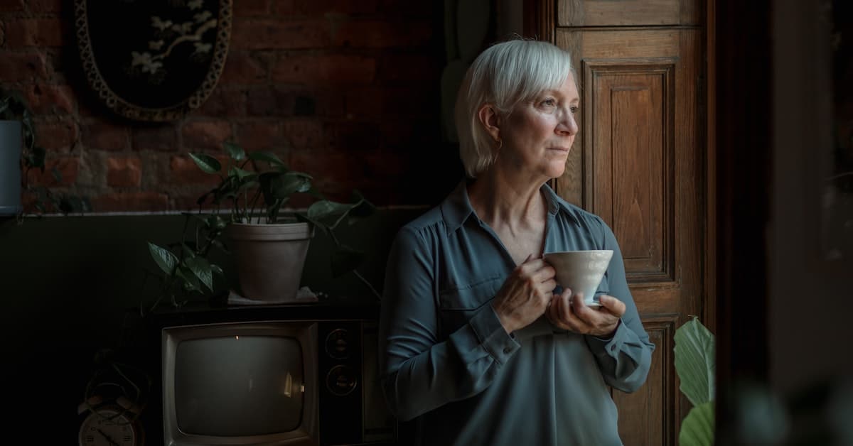 older woman looking out window with coffee cup thinking about social security benefits from ten years of marriage