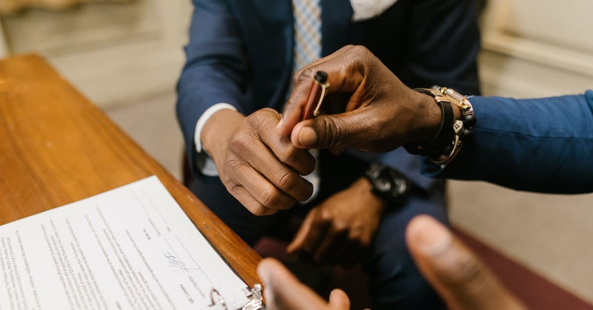 two people passing pen to sign paperwork for divorce with lawyers representing each party