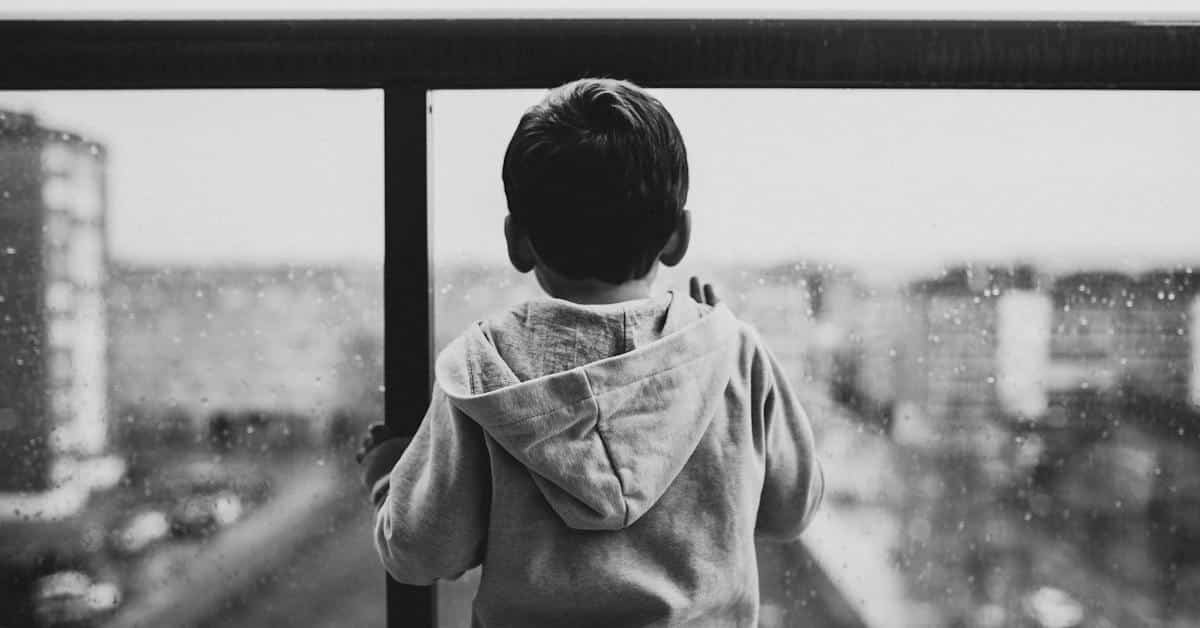black and white photo of a kid looking through a window whose parent quit their job to reduce child support